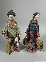 Front view of two Shiwan Wucai porcelain figurines displaying attire, child, lanterns, peppers