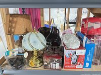 Shelf view showing lamps, growler, tractor figurine, iron box, faux-flower cluster