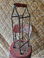Full front view of black metal wine rack showing four circular holders and wood handle
