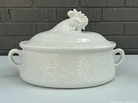 Front view of covered casserole showing rooster finial and handles
