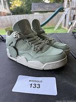 Left side view of the sage green Air Jordan 4 sneakers size 7 on tabletop