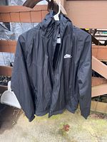 Front view of black Nike hooded windbreaker hanging on hanger showing full-zip front and swoosh logo