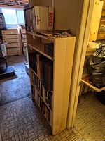 Side view of tall wooden bookshelf filled with books, showing full height and five shelves