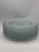 Stack of ten clear pressed glass platters showing uniform size and pattern