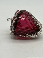 Side view of ruby red glass strawberry paperweight showing clear glass seed textures and leaf detail