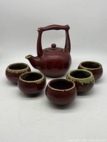 Front view of red stoneware teapot and five cups