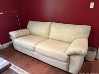 Front view of white leather three-seat pull-out sofa against red wall