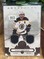 Front of Bergeron Artifacts dual jersey card showing player image, two black swatches, serial number 118/165