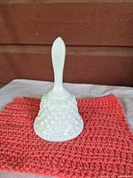Front view of white milk glass hobnail bell on cloth