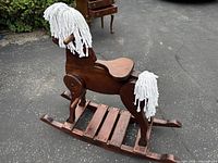 Left side view of wooden rocking horse showing platform rocker, saddle, mane, tail