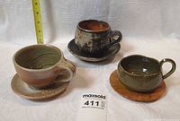 Three stoneware cups each on a saucer, measuring tape for scale