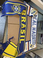 Both scarves flat on box, showing Brasil scarf full and part of Real Madrid