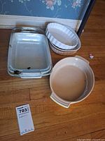 All four baking pieces arranged on floor: glass baker, glass lid, fluted pie dish, Le Creuset casserole