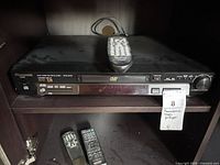Panasonic DVD-RV31 player on shelf with three remotes