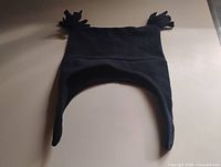 Full view of black fleece ear-flap hat laid flat