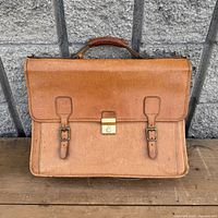 Front view of briefcase showing flap, buckle straps, brass lock, handle
