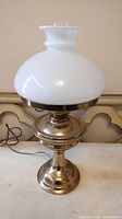Full view of brass table lamp with white milk glass globe shade and plug cord visible