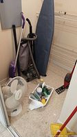 Closet view showing Kirby vacuum, Cool Works fan, ironing board, mop, dustpan, cleaning caddy with bottles