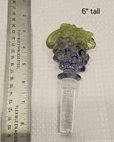 Grape-motif crystal wine stopper beside ruler showing 6-inch length