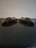Two amber glass car-shaped bottles side by side on dark surface