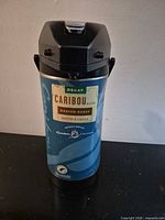 Front view of Caribou Coffee airpot showing blue body and pump lid