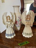 Two ceramic angel figurines with musical instruments and floral vase on wooden surface
