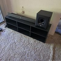 Soundbar resting on six-cubby black media console with wireless subwoofer beside