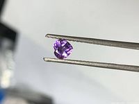Heart-cut amethyst held by tweezers, showing overall shape and color