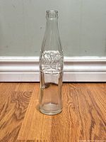 Full view of clear glass Coca-Cola contour bottle standing upright