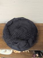 Top view of black pillbox hat showing gathered net veil on crown