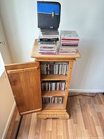 Full view pine CD cabinet with open door, shelves of CDs, stacked CDs and wallet on top