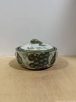 Side view of covered casserole showing painted fruit motif and overall condition