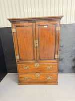 Full front view of oak tansu-style cabinet showing doors, drawers, brass hardware