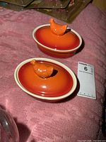 Pair of orange ceramic hen-on-nest dishes with lids displayed together