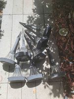 Eight grey solar path lights with clear glass shades lying on paving