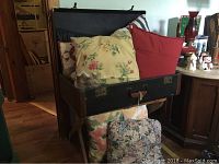 Vintage black suitcase on wooden stand filled with colorful floral cushions and pillows.