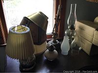 Main photo of lamps and shades on table including oil lamps with glass chimneys and several lamp shades