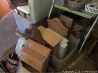 Unpainted wooden boxes with shaped tops stacked in a bin with other craft materials and wood supplies.