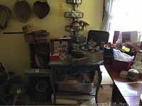 Wide view of the craft items arranged on and under tables showing baskets, boxes, paints, and decorative pieces.