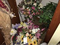 Long view of multiple artificial floral arrangements and greenery grouped closely together, showing flower variety and containers.