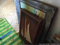 Overall view showing the sailboat framed wooden relief artwork leaning against a wall among other frames.