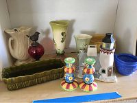Shelf with two Hull pottery vases, lighthouse piece, green planter, blue bowl, candlesticks, red bird figurine, and cream vase.