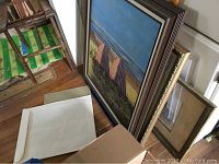 Large framed painting showing two striped beach tents on sandy dunes with blue sky, leaning against a wall