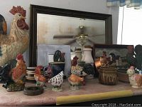 Wide view of rooster decor arrangement on shelf with mirror at back, multiple rooster figurines, ceramic jars, plates, and tray