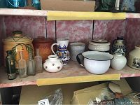 Shelf of various pottery jugs, bottles and an enamel coated pot showing wear on rim.