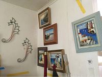 Seven pieces of nautical-themed wall art consisting of five framed paintings depicting seaside scenes and two green metal seahorses mounted on wall.