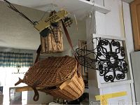 Photo of hanging rustic decor including wooden garden seeds planter box, wicker fishing basket, and metal scroll wall hanging