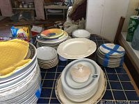 Wide view showing multiple stacks of plates and dishware including yellow textured plates, white plates, small bowls, and colorful plates.