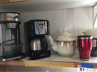 Two coffee makers: Hamilton Beach and Mr. Coffee, a ceramic teapot with floral print, and a red travel mug on a wooden shelf.