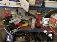 Shelf containing assorted hand tools, tubes of adhesive, paint cans, and small hardware items